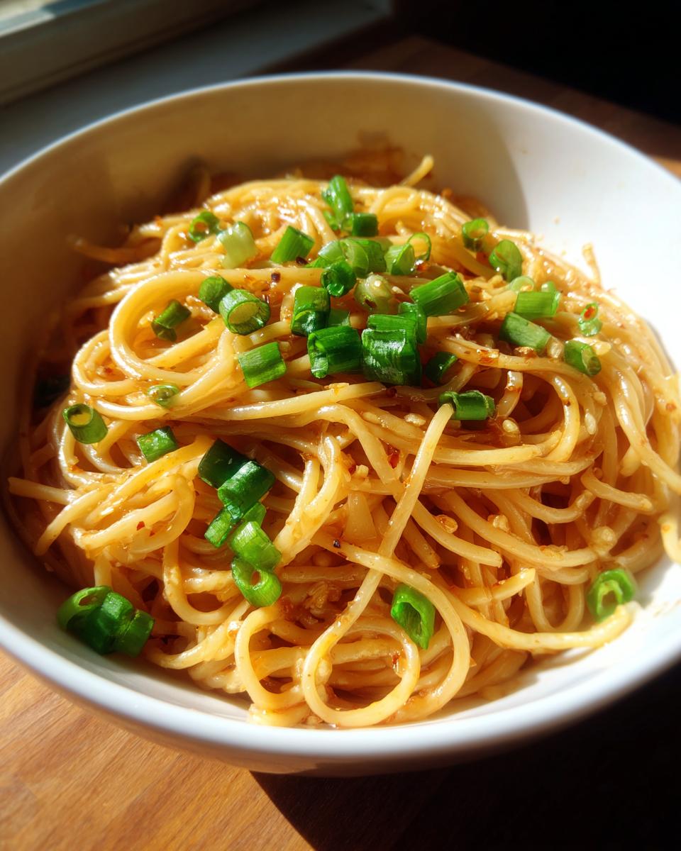 A bowl of glistening 15-minute garlic noodles, topped with fresh chopped green onions.