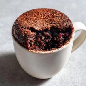 A single-serving Cottage Cheese Microwave Brownie in a white mug, topped with cocoa powder.