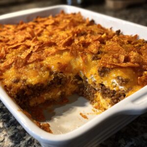 Close-up of a cheesy Dorito Casserole in a white baking dish, showing layers of beef and Doritos.