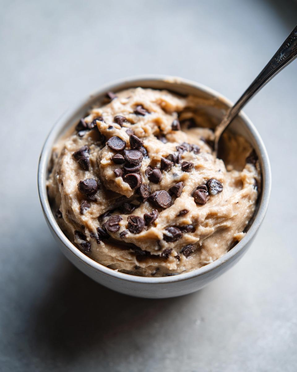 A bowl of creamy high protein cookie dough with chocolate chips, ready to eat with a spoon.