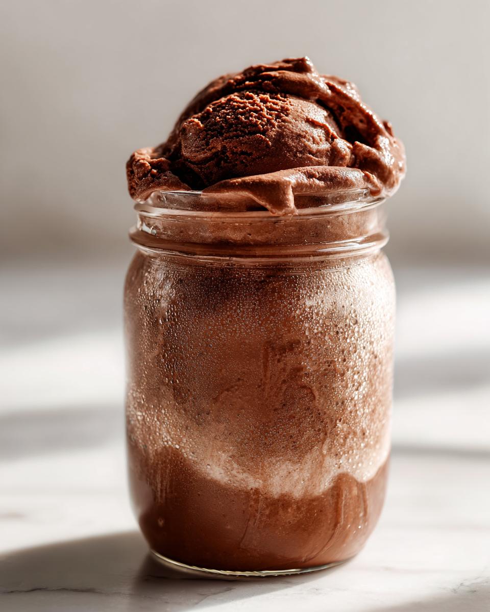 A full mason jar of homemade mason jar chocolate ice cream with a scoop on top.