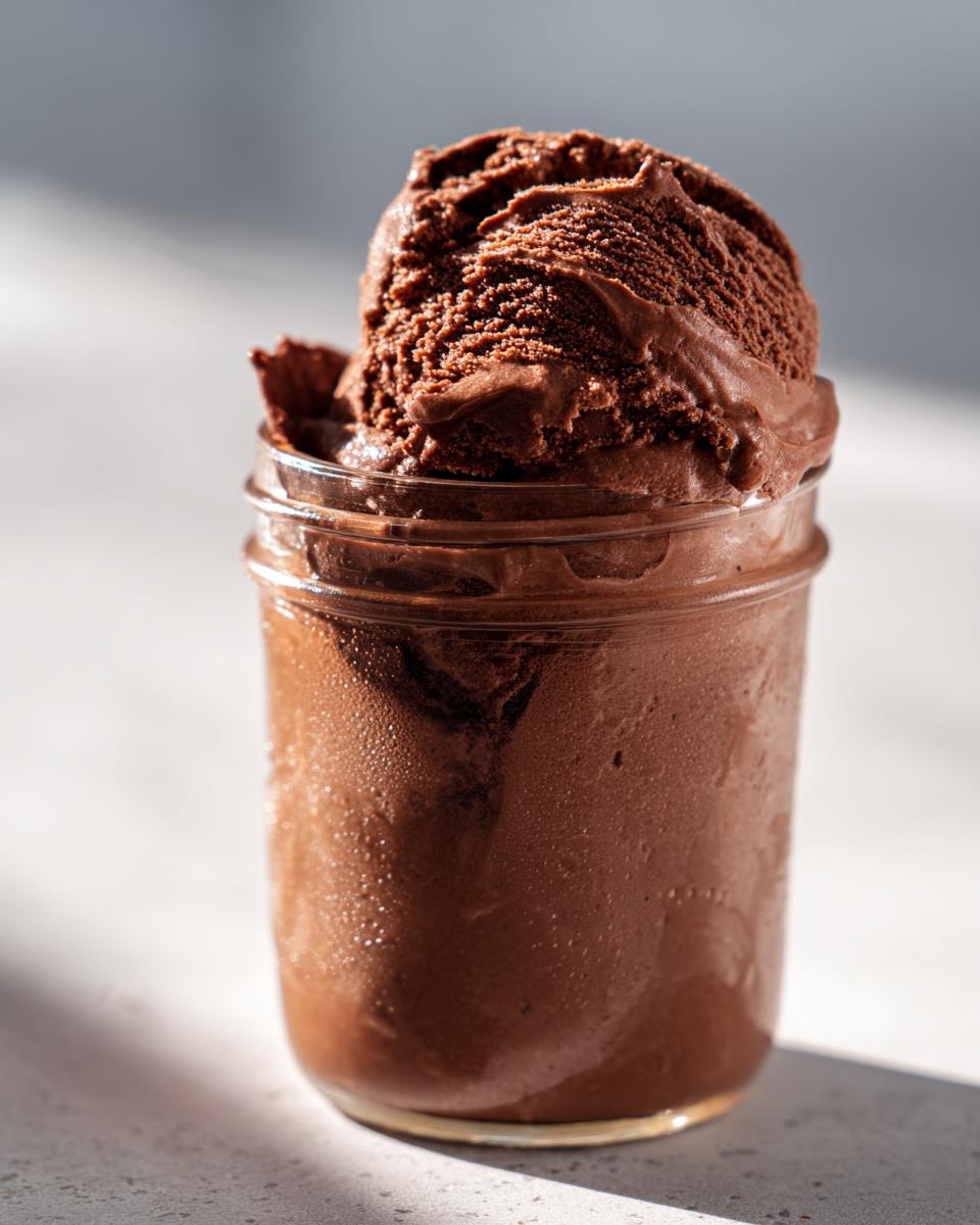 A scoop of rich mason jar chocolate ice cream in a glass jar, showing its smooth texture.