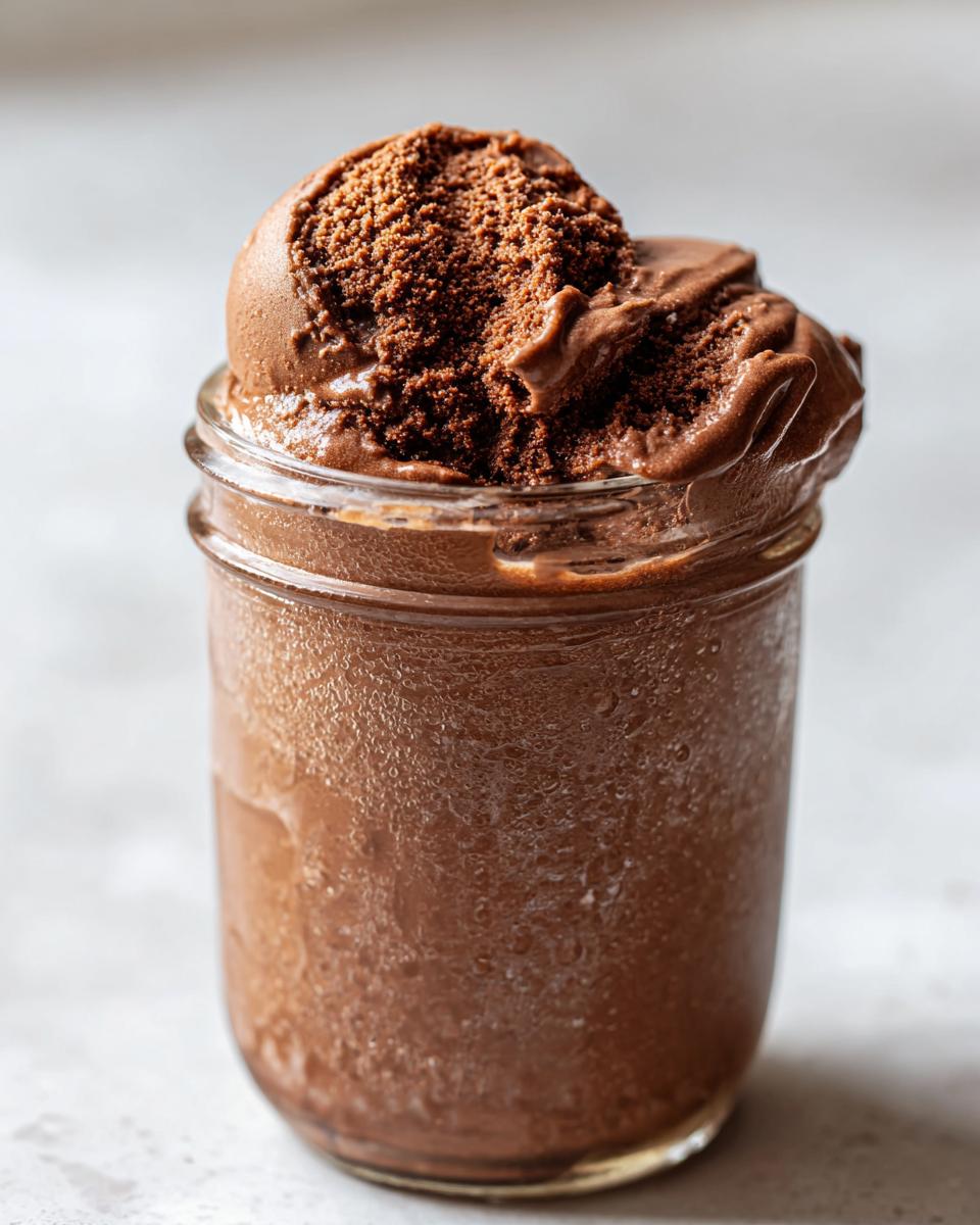 Close-up of homemade Mason jar chocolate ice cream in a glass jar with condensation.