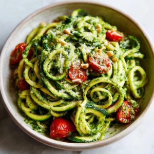 A bowl of vibrant zucchini noodle pesto salad with cherry tomatoes, pesto, and parmesan cheese.