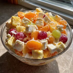 A vibrant Ambrosia fruit salad in a glass bowl, featuring oranges, pineapple, grapes, marshmallows, and coconut.