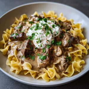 A bowl of delicious Beef Stroganoff with egg noodles, topped with sour cream and fresh parsley.