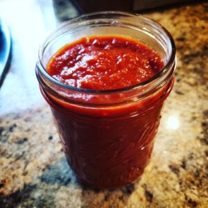 Close-up of homemade canned tomato sauce in a glass jar, ready for canning.