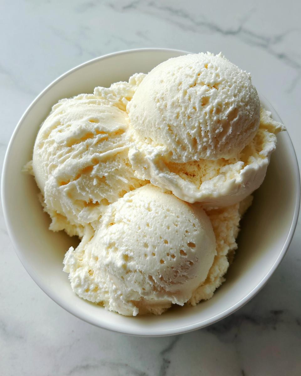A white bowl filled with three scoops of creamy, homemade cottage cheese ice cream.