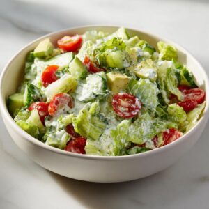 A vibrant bowl of Green Goddess Chopped Salad featuring lettuce, tomatoes, cucumber, and avocado with creamy dressing.