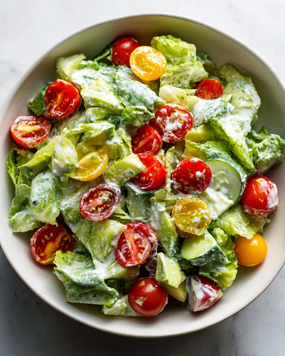 Overhead view of a Green Goddess Chopped Salad in a bowl with lettuce, tomatoes, cucumber, and creamy dressing.