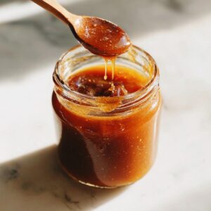 A jar of homemade apple butter with a wooden spoon dripping the rich, spiced spread.