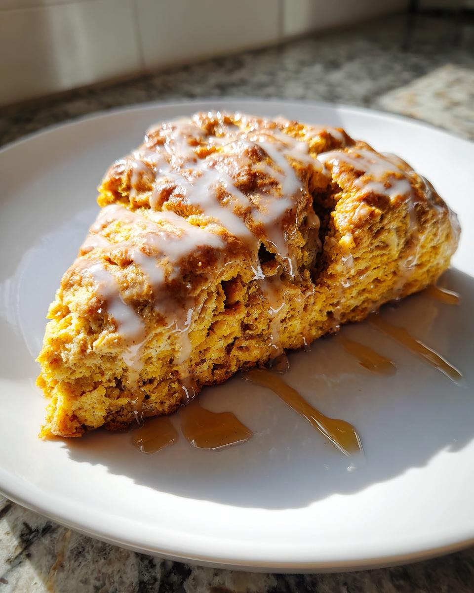 A glazed maple pumpkin scone on a white plate, drizzled with maple syrup.