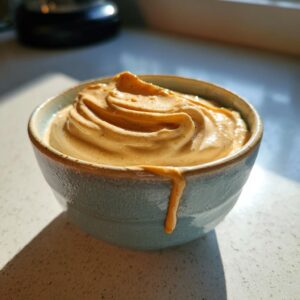 A bowl of creamy peanut butter yogurt dip, with a drip down the side, sitting on a white surface.