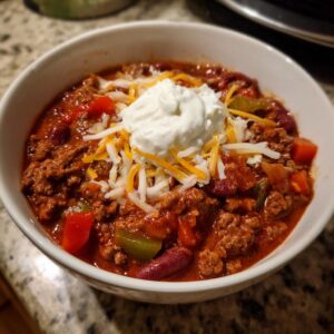 A bowl of hearty slow cooker chili topped with sour cream and shredded cheese.