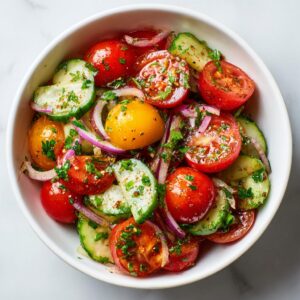 Overhead shot of a vibrant Tomato cucumber salad with red onion and herbs in a white bowl.