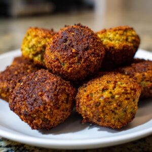 Close-up of a pile of golden-brown, crispy falafel balls on a white plate.