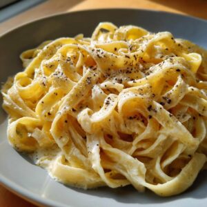 Close-up of a plate of delicious Fettuccine Alfredo pasta coated in a rich, creamy sauce and sprinkled with black pepper.