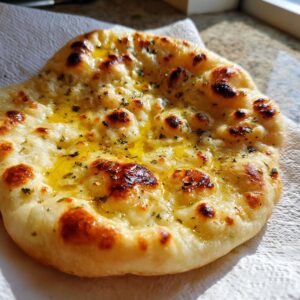 Close-up of a freshly baked, soft and chewy naan bread brushed with melted butter and herbs.
