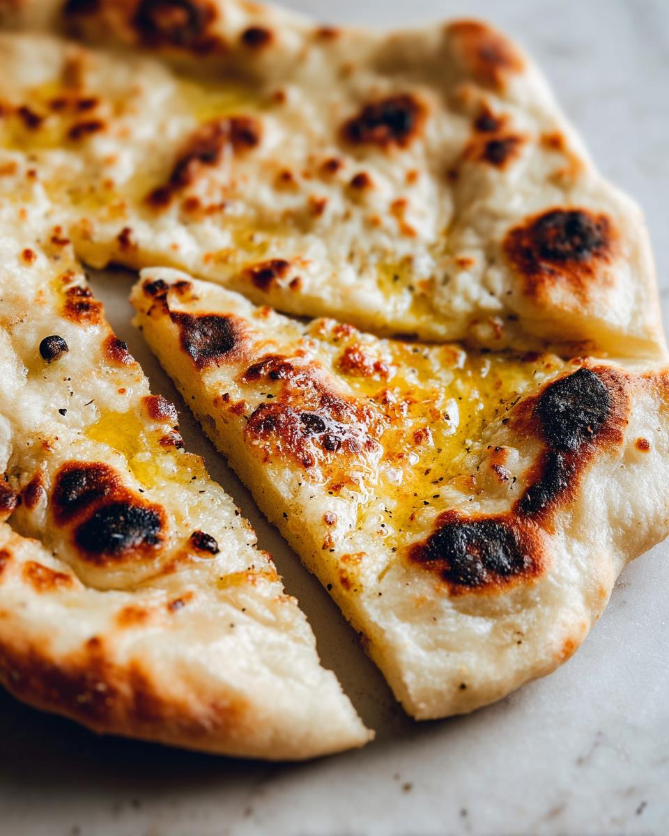 Close-up of freshly baked, soft, and chewy naan bread brushed with melted butter and spices.