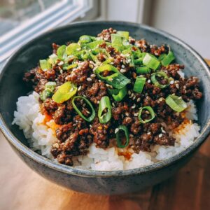 Close-up of a Korean Beef Bowl with seasoned ground beef over white rice, topped with green onions and sesame seeds.