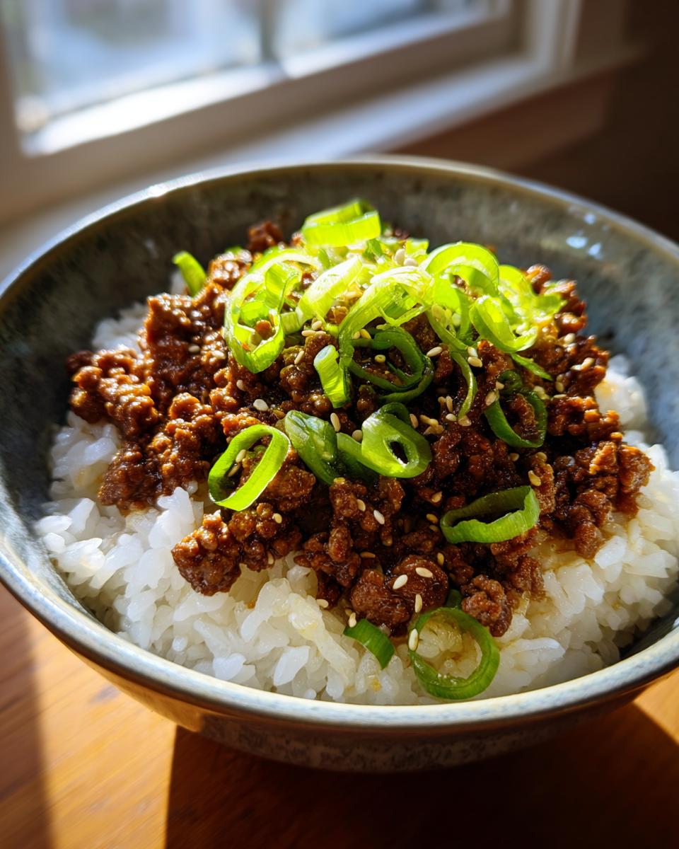 Close-up of a bowl of Korean Beef Bowls, featuring seasoned ground beef over white rice, topped with fresh scallions and sesame seeds.