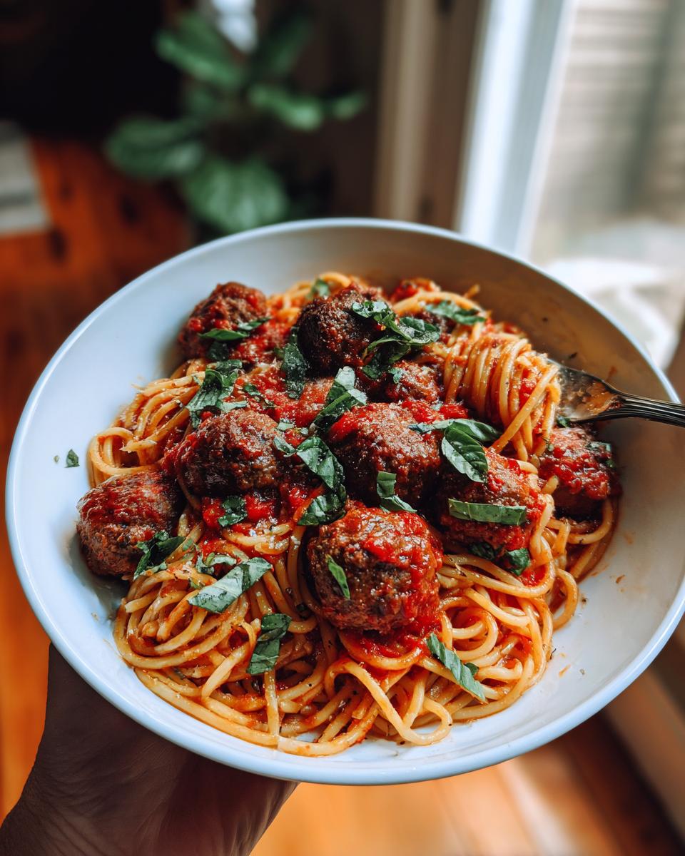 A close-up of a bowl of spaghetti and meatballs, topped with marinara sauce and fresh basil.