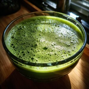 Close-up of a vibrant green Witches' Brew Punch with a foamy top in a clear glass bowl.