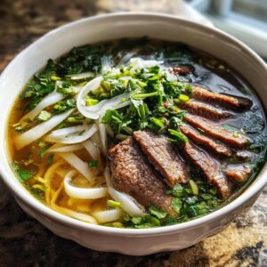 A close-up of a steaming bowl of beef Pho, showcasing tender slices of beef, rice noodles, fresh cilantro, and thinly sliced onions in a rich broth.