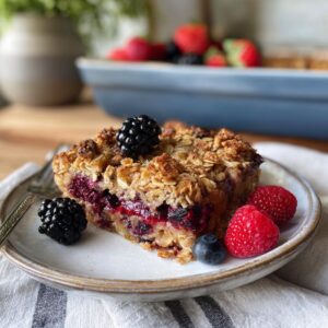 A delicious slice of berry baked oatmeal topped with fresh blackberries, raspberries, and blueberries.