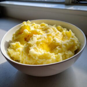 A white bowl filled with fluffy, creamy mashed potatoes topped with melted butter.