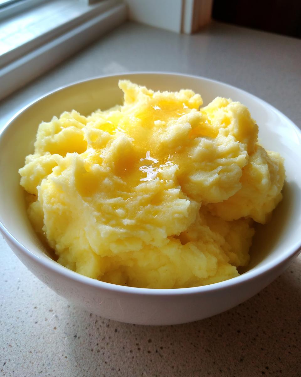 A close-up of a white bowl filled with fluffy, creamy mashed potatoes topped with melted butter.