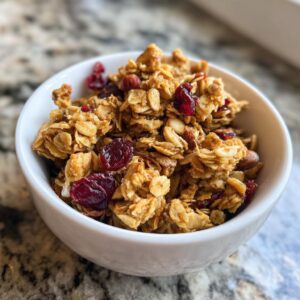 A white bowl filled with homemade granola, featuring crunchy clusters, dried cranberries, and almonds.