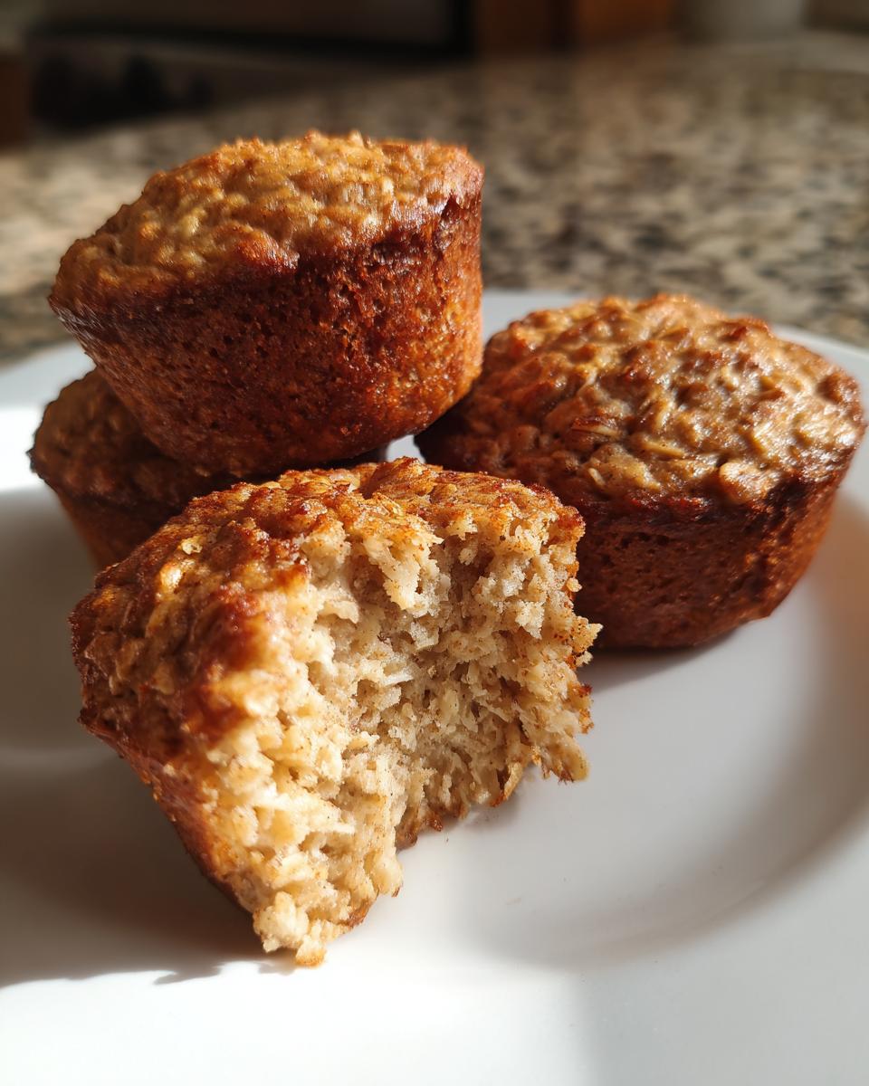 A close-up of delicious oatmeal muffins, with one muffin bitten into, revealing a fluffy interior.