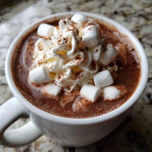 A close-up of a mug filled with rich hot chocolate, topped with whipped cream, marshmallows, and a sprinkle of cinnamon.