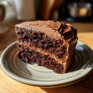 A decadent slice of moist chocolate cake with rich chocolate frosting, served on a plate.