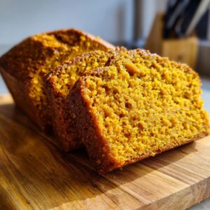 Close-up of moist pumpkin bread slices on a wooden cutting board, showcasing the rich orange color and texture.