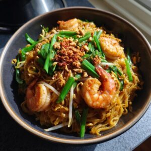 A close-up of a bowl of Pad Thai with shrimp, bean sprouts, green onions, and crushed peanuts.