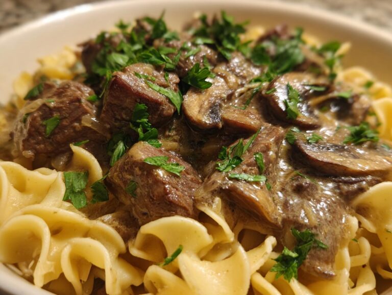 A close-up of slow cooker beef stroganoff served over egg noodles, garnished with fresh parsley.