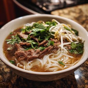 A close-up of a steaming bowl of authentic beef pho, featuring tender beef slices, rice noodles, fresh herbs, and bean sprouts.