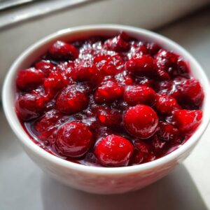 Close-up of vibrant, glistening homemade cranberry sauce in a white bowl, showcasing whole cranberries.