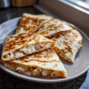 Close-up of golden-brown chicken quesadilla slices filled with shredded chicken and melted cheese.