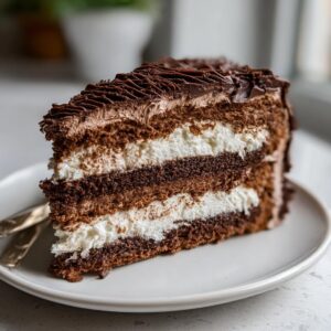 A decadent slice of chocolate Yule log cake with layers of chocolate cake and cream filling, topped with chocolate frosting.