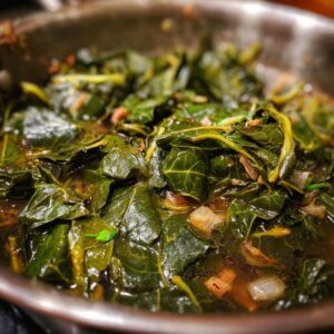 Close-up of tender, wilted collard greens simmering in a pot with onions and broth.