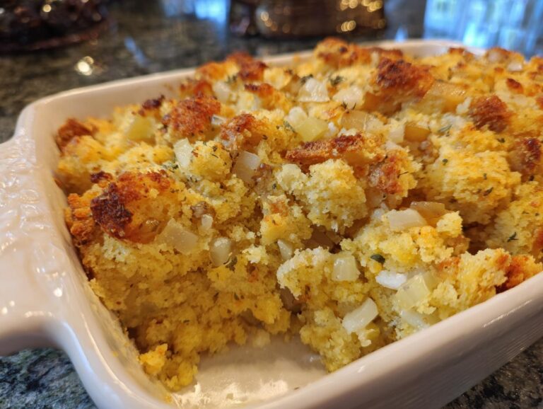 Close-up of a freshly baked cornbread dressing in a white baking dish, showing golden brown crust and visible pieces of onion.