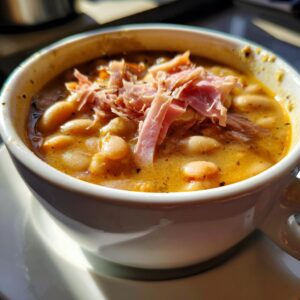 Close-up of a rich, creamy Ham and bean soup topped with shredded ham, served in a white mug.