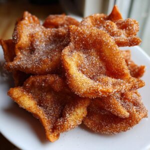 A close-up of freshly fried Buñuelos dusted heavily with sparkling cinnamon sugar on a white plate.