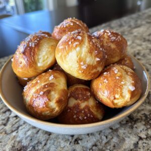 A close-up bowl overflowing with golden brown soft pretzel bites, sprinkled with coarse salt.