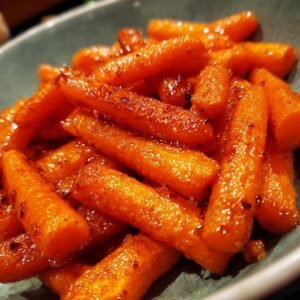 A close-up shot of a bowl filled with glistening glazed carrots, showcasing their vibrant orange color and sweet coating.