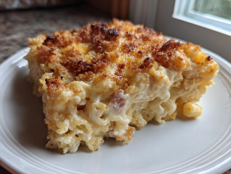 A thick slice of creamy Ham and Cheese Casserole featuring elbow macaroni, visible ham pieces, and a golden-brown, crispy topping.