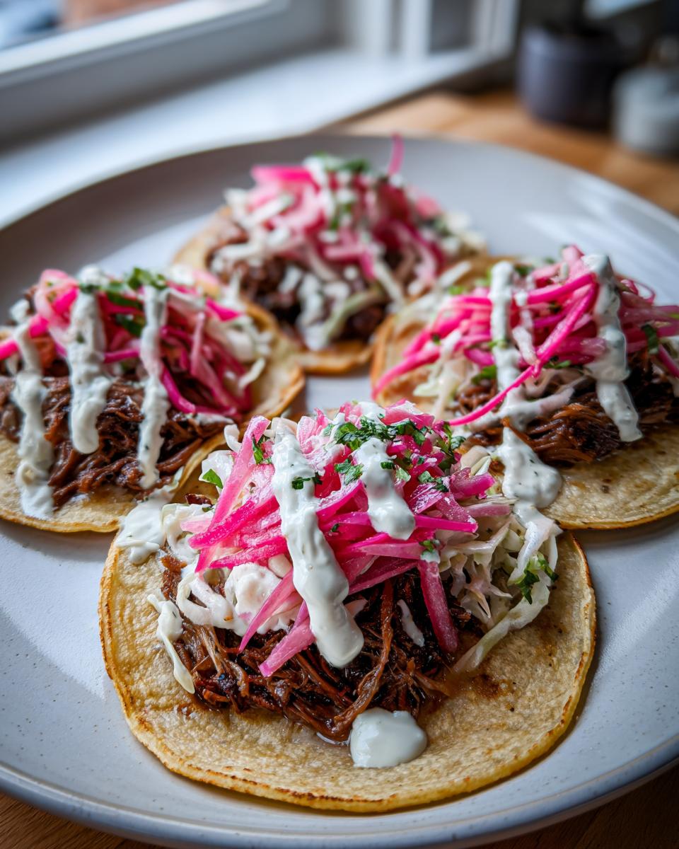 Four delicious Hanukkah brisket tacos topped with slaw, pickled onions, and white sauce on a light plate.